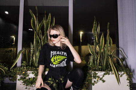 Modelka prezentuje czarną koszulkę zespołu health nature pikers i mfc młody bóg na tle roślin doniczkowych